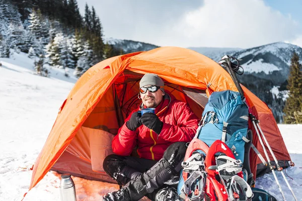冬のテント近くマグカップから男の飲み物 テント バックパック 山の背景に棒やスノー シューズを追跡します 雪の中でキャンプ アクティブな休息と冬期登山 — ストック写真