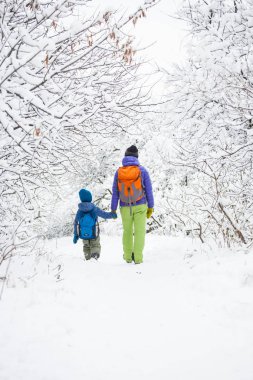Çocuk annesiyle bir orman karla kaplı yolda yürür. Kış tatili. Bir sırt çantası olan bir çocuğun annesi ile eğleniyor.