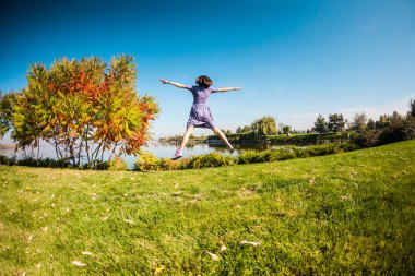 Elbiseli bir kız bir yeşil çayırlarda çalışır. Parkta yürüyen kadın. Doğa etkinliğinde. İnce esmer eğleniyor. Kız çimlere atlama.