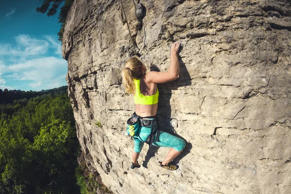 The girl climbs the rock. A woman is engaged in fitness in nature. Extreme sport. Climbing route. Preparation for competitions. Achieving the goal. Effort to complete the task. Workout.