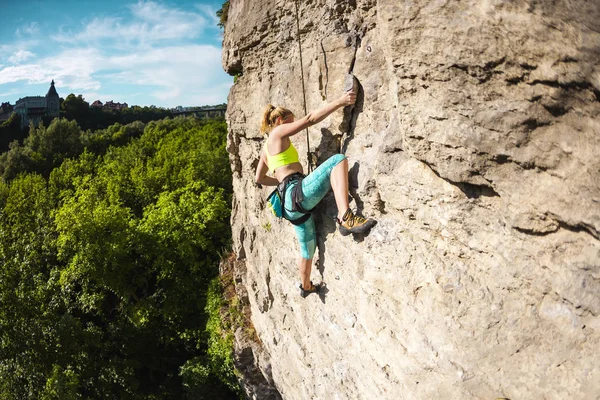 The girl climbs the rock. A woman is engaged in fitness in nature. Extreme sport. Climbing route on natural terrain. Endurance training. Workout.