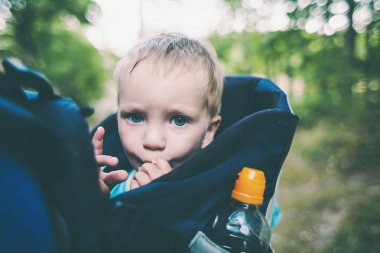 Bir çocuk bir sırt çantası içinde oturuyor. Bir çocuk portresi. Çocuk ailesiyle birlikte dolaşıyor. Bir çocukla tırmanma. İlginç çocukluk. Bir bebek taşıyan baba. Bebek gülümsüyor.