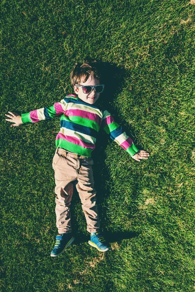 少年は 草の上に横たわっています 緑の芝生の上面に休んでいます 芝生の上楽しんで子供 — ストック写真
