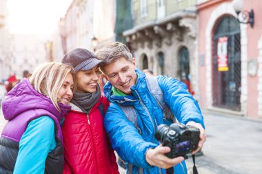 Arkadaşlar bir selfie al. Üç arkadaş güzel eski kasabanın içinden yürüyorlar. Avrupa şehirlere seyahat. İki kadın ve bir adam eski binalar fonunda fotoğraflandı.