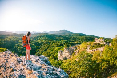 Dağın zirvesine kıza. Bir kadın bir sırt çantası ile bir kaya üzerinde duruyor. Yukarı tırman. Güzel yerlere seyahat. Turist gökyüzünün ve denizin karşı. Ufuk esmer bakar.