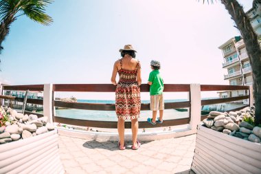 Kadın bir çocukla denizde bak. Çocuk annesiyle birlikte sahile gidiyor. Tatil beldesinde bekletin. Limanda sokak yürüyün. Liman. Sahile çit. Balık gözü lens.