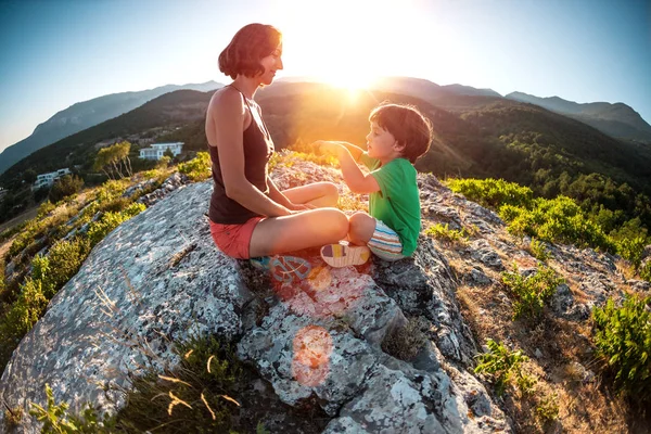 A woman is traveling with a child. Mother with a son is sitting on a large rock. Climb to the top of the mountain with children. The boy with the backpack climbed to the top. Active vacations.