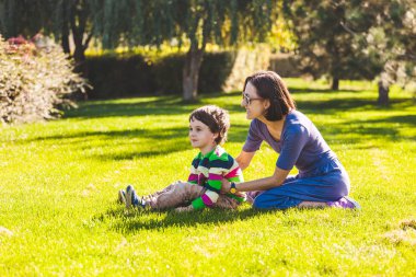 Çocuk annesi ile yeşil çimenlerin üzerinde oturuyor. Çocuk anne-baba ile parkta yürüyor. Annenin sarılmalar. Bir kadının oğlu doğa ile eğleniyor.