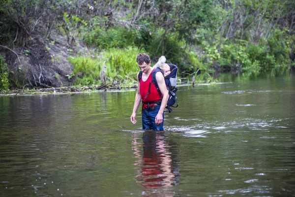 子供を持つ男は 川を横切る 息子をバックパックで運びます 洪水から救出します アジアにおける洪水犠牲者の避難 ジャングルの中を子供と一緒に旅行 極端な観光 — ストック写真