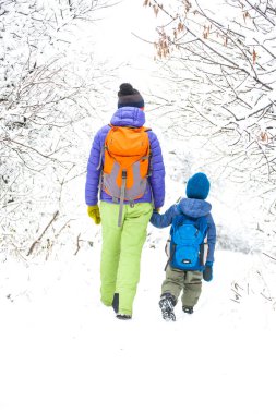 Çocuk annesiyle bir orman karla kaplı yolda yürür. Kış tatili. Bir sırt çantası olan bir çocuğun annesi ile eğleniyor.