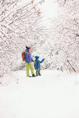 Çocuk annesiyle bir orman karla kaplı yolda yürür. Kış tatili. Bir sırt çantası olan bir çocuğun annesi ile eğleniyor.