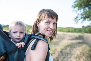 Bir oğlan bir sırt çantası içinde oturuyor. Çocuk ailesiyle birlikte dolaşıyor. Bir çocukla tırmanma. Anne Bebek taşır. Küçük bir seyahat. Bir kadın bebeğini taşıyor. Çocuklarla seyahat.