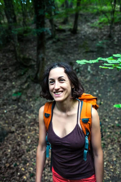 The girl is walking through the forest. A young woman with a backpack travels through picturesque places. A tourist walks along a mountain path.