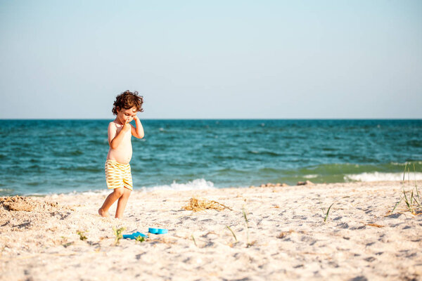 Мальчик играет с песком на морском пляже. Ребенок бежит по побережью против неба. Ребенок веселится на природе. Мальчик в отпуске.
.