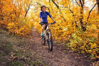 Bir sırt çantası ile kız sonbahar parkta bisiklete biniyor. Doğada ince kadın trenler. Ormanda spor. Turistik bir kir iz sürmek. Bisikletle seyahat.