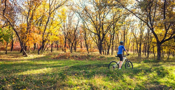 The girl with a backpack rides a bike in the autumn park. Slender woman trains in nature. Sports in the forest. Tourist rides on a dirt trail. Traveling by bike.