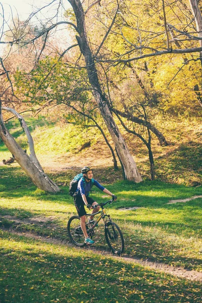 The girl with a backpack rides a bike in the autumn park. Slender woman trains in nature. Sports in the forest. Tourist rides on a dirt trail. Traveling by bike.