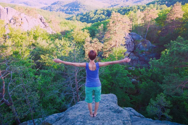 girl engages in yoga on the top of mountain, solitude with nature and meditation on grief. healthy way of life. A woman stands on a rock with her arms wide apart.