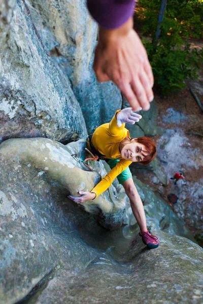 Rock-climber gives five. The girl overcomes a difficult climbing route. A woman goes in for sports on nature with friends.