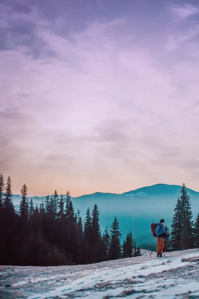 冬の山の背景にバックパックを持つ男 クライマーは 夜明けを満たしています 山の中の冬の登頂 夕日の光線 上の日没 — ストック写真