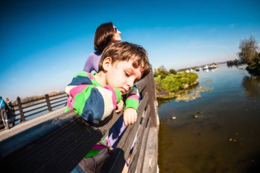 Oğlan ve annesi köprünün korkuluk, ayakta duruyorlar. Bir çocuk annesi Park ile yürür. Bir kadın oğluyla nehirde arıyoruz.