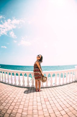 Kız sahilde standları ve denizde görünüyor. Bir kadın limanda sokak yürür. Esmer elbiseli okyanus kıyısında dinlenme. Balkon korkuluk. Kızı sahile gidiyor. Balık gözü lens.