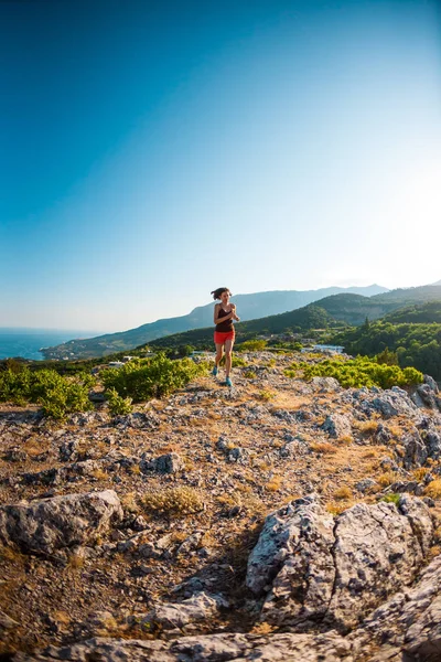 A girl is running in the mountains. A woman goes in for sports in nature. Slender brunette on top of a mountain. Skyrunning.