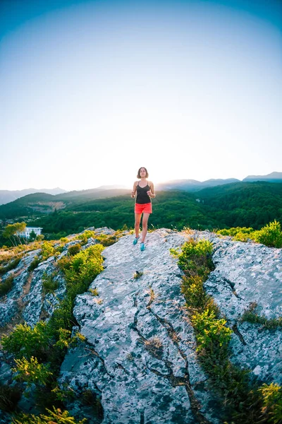 A girl is running in the mountains. A woman goes in for sports in nature. Slender brunette on top of a mountain at sunset. Skyrunning.