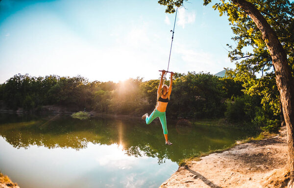Прыгай в воду. Женщина отдыхает на озере. Качели из веревки и палки. Активный отдых на природе. Летнее веселье. Женщина качается на качелях. Объектив Fisheye
.