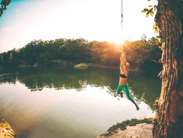 Jump into the water. A woman is resting on the lake. A swing from a rope and a stick. Active recreation in nature. Summer fun. A woman is riding a swing. Fisheye lens.