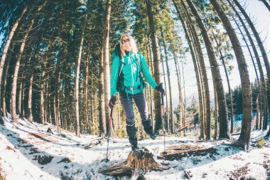 Kış dağlarında sırt çantalı ve kar ayakkabılı bir kadın. Manzaralı yerlere git. Yürüyüş sopalı bir sarışın. Karlı bir ormanda bir turist yürüyor. Kız eğleniyor..