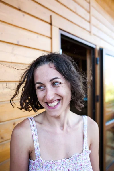 Portrait of a laughing woman. Smiling girl. Emotions of joy. Brunette on the background of a wooden house. A woman is resting on the veranda at home. A face without makeup.