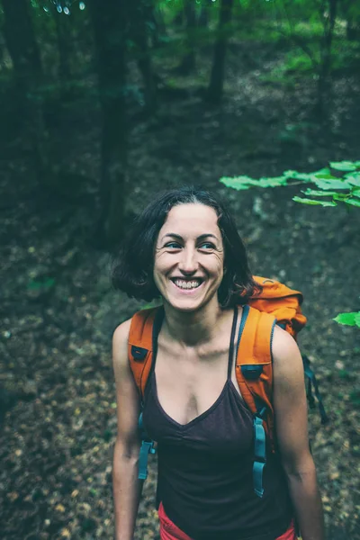 The girl is walking through the forest. A young woman with a backpack travels through picturesque places. A tourist walks along a mountain path.