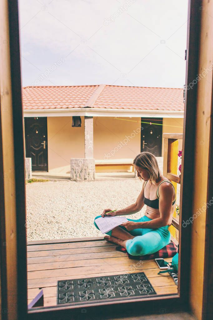 Portrait of a thoughtful woman. Emotions of calm and reverie. Blonde on the background of a wooden house. A woman is resting on the veranda at home.  The girl writes on a sheet of paper.