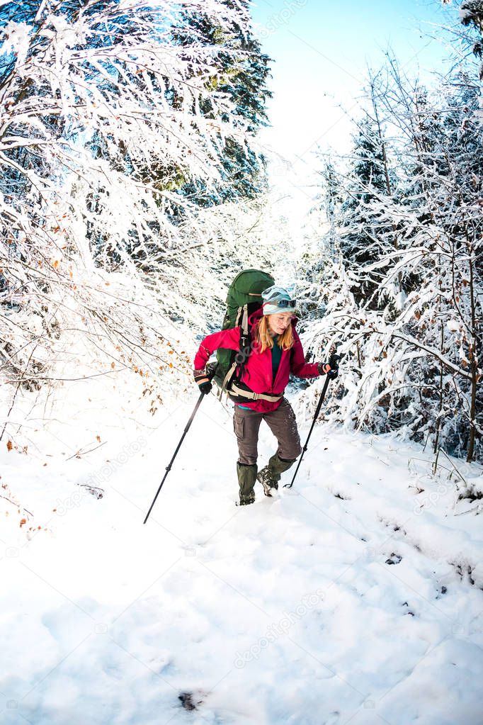 Woman with backpack and snowshoes in the winter mountains. Travel to scenic places. Blonde with trekking sticks. A tourist walks through a snowy forest. Girl walks along the path.