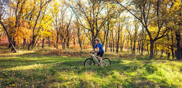 The girl with a backpack rides a bike in the autumn park. Slender woman trains in nature. Sports in the forest. Tourist rides on a dirt trail. Traveling by bike.