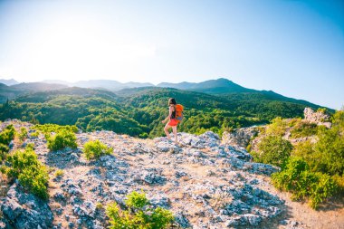 Dağın zirvesine kıza. Bir kadın bir sırt çantası ile bir dağ yolunda yürüyor. Yukarı tırman. Güzel yerlere seyahat. Gökyüzü ve deniz karşı Turizm.
