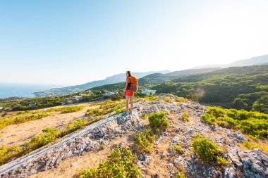 Dağın zirvesine kıza. Bir kadın bir sırt çantası ile bir dağ yolunda yürüyor. Yukarı tırman. Güzel yerlere seyahat. Gökyüzü ve deniz karşı Turizm.