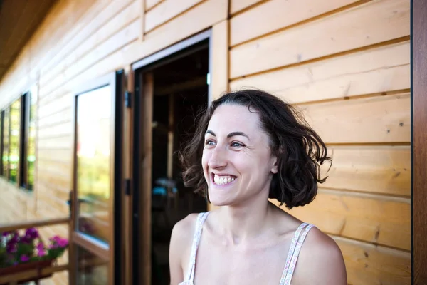 Portrait of a laughing woman. Smiling girl. Emotions of joy. Brunette on the background of a wooden house. A woman is resting on the veranda at home. A face without makeup.