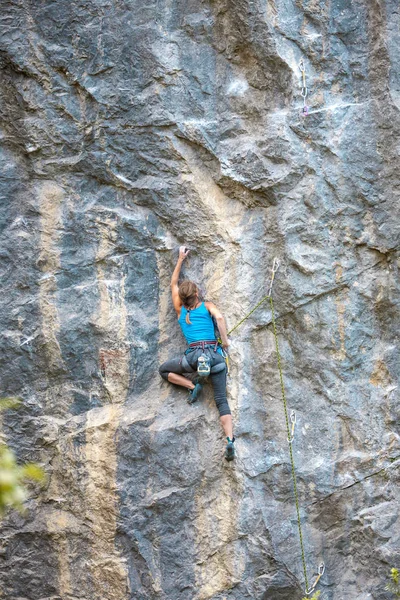 The girl climbs the rock. The climber is training to climb the rock. A strong athlete overcomes a difficult climbing route. Extreme hobby. A woman goes in for sports in nature. Natural rocky terrain.