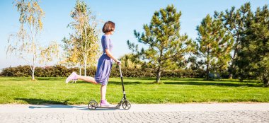 Kız ile bir scooter parkta gidiyor. İçinde ince kadın iyi eğlenceler. Yürüyüşe gülümseyen esmer.