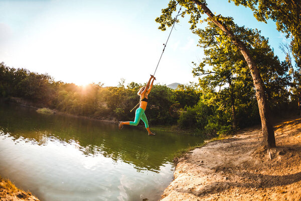 Прыгай в воду. Женщина отдыхает на озере. Качели из веревки и палки. Активный отдых на природе. Летнее веселье. Женщина качается на качелях. Объектив Fisheye
.