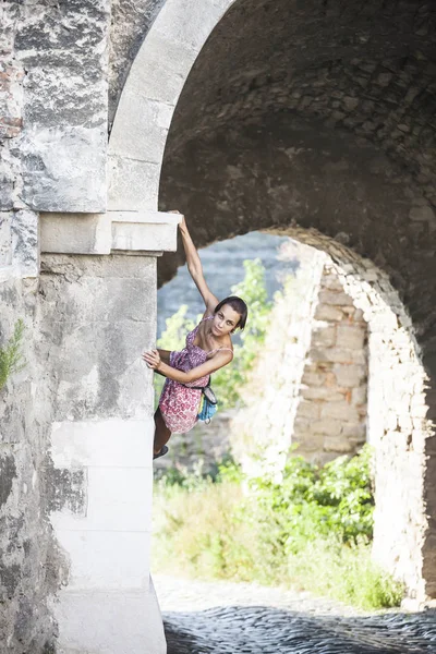 The girl climbs the stone wall. A woman in a summer dress climbs the wall of an old destroyed building. Brick fence. The climber is hanging on the city building. Strengthening the ruined castle.