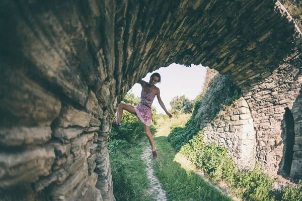 The girl climbs the stone wall. A woman in a summer dress climbs the wall of an old destroyed building. Brick fence. The climber is hanging on the city building. Strengthening the ruined castle.