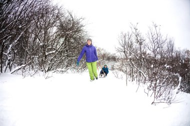 Bir kadın bir çocuk bir kızağa alır. Bir çocuk annesi kış ormanı ile yürür. Çocuk ile bir kızakta kar üzerinden gidiyor. Kış tatili. Anne ile eğlenceli eğlence.