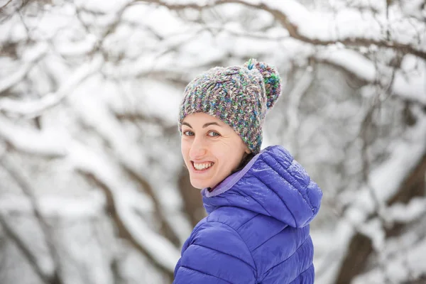 一个戴针织帽子的女人的肖像 微笑的女孩走过冬天的森林 褐发女郎在雪树的背景 — 图库照片