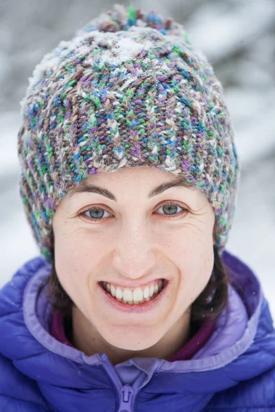 ニット帽子の女性の肖像画 微笑んでいる女の子は冬の森を歩きます 雪に覆われた木の背景にブルネット — ストック写真
