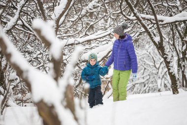 Çocuk annesiyle bir kar kaplı orman yolu üzerinde yürür. Kış tatili. Bir çocuk annesi ile eğleniyor.