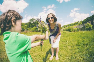 Çocuk annesinin anneler gününde kutladı. Bir kadın ve oğlu bir çayır bir yürüyüş mesafesindedir. Çocuk annesi bir buket çiçekler verir. Doğum günü hediyesi.
