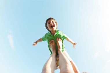 Boy gülümseyerek bir uçak gibi annemin bacaklarına uçar. Çocuk gökyüzüne karşı. Çocuk ve annesi çifti Yoga doğada nişanlandık. Bir kadın oğlunu eğlendirir. Acro yoga.